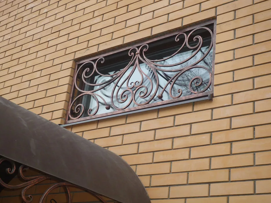 Окно с кованой решеткой на кирпичной стене.